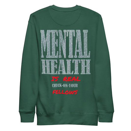 Close-up of a graphic print on a green hoodie, showcasing sparkling letters spelling out "MENTAL HEALTH IS REAL" with a striking red phrase below, urging viewers to check on their friends. The design promotes a positive message about mental health.