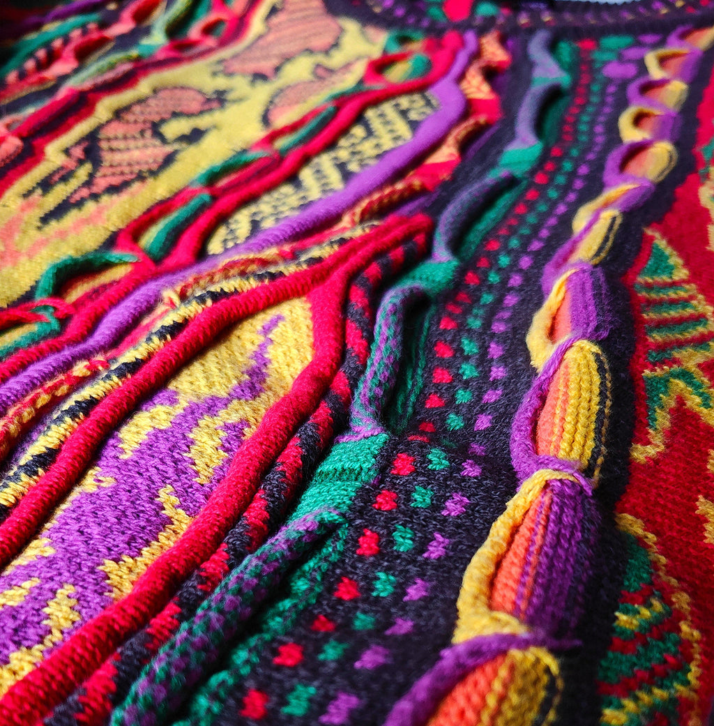 Macro view of the knit: raised cables, zigzag and diamond jacquard fields in magenta, red, yellow, green and aubergine