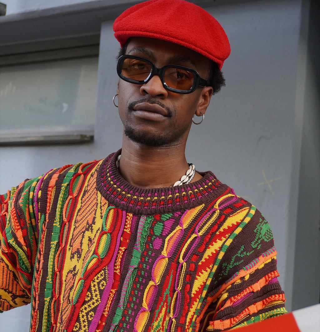 Close portrait showing the ribbed collar of the 3D knit sweater, colour-shifting rib with yellow flecks, worn with an orange Mainey More beanie
