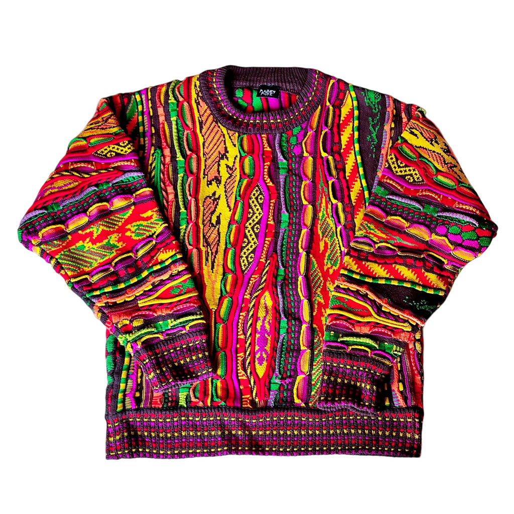 Model in an oversized 3D knit sweater with raised cables and jacquard panels in magenta, red, yellow, green and aubergine